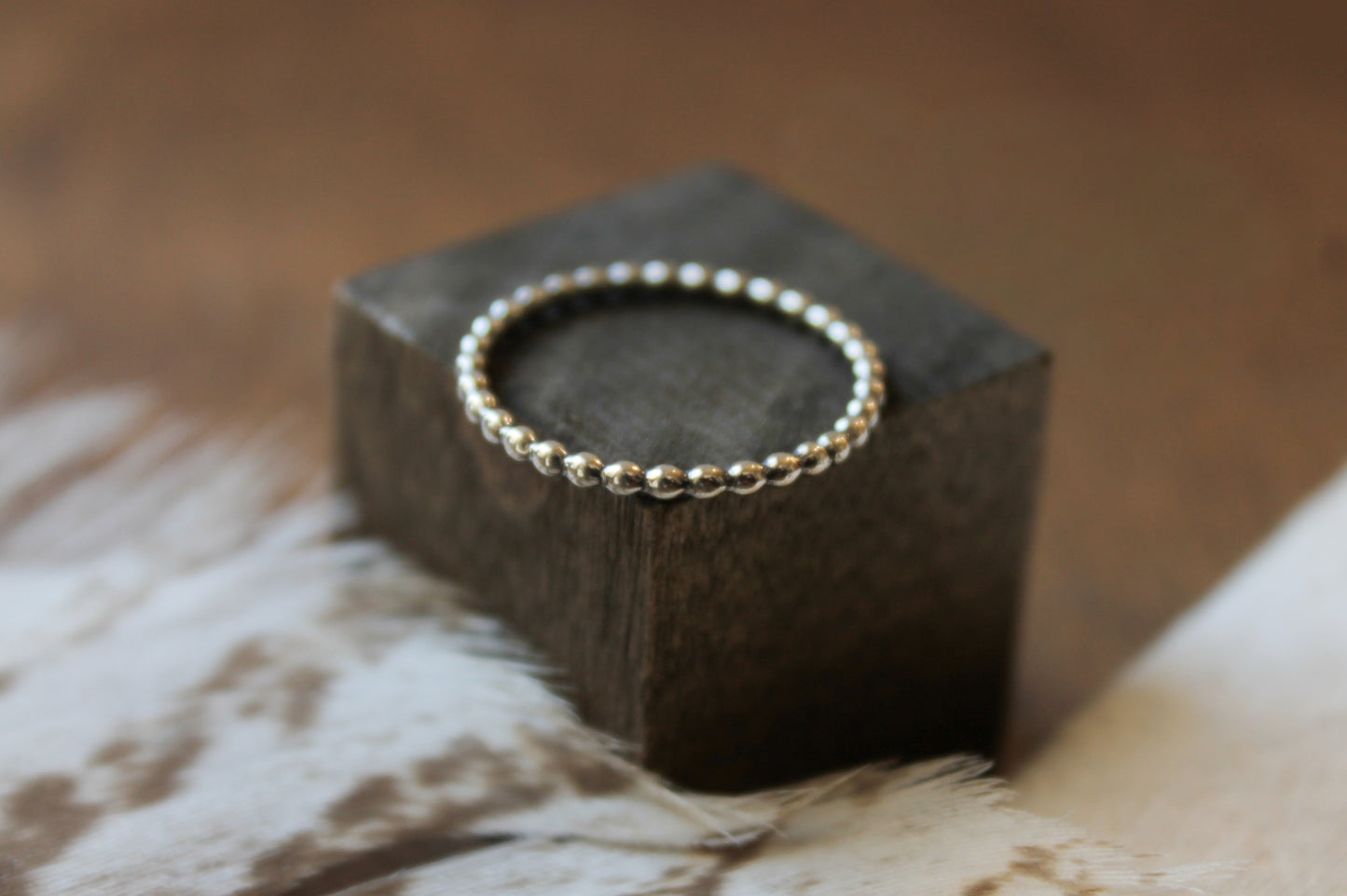 Sterling silver beaded ring on a dark wooden block with a blurred background
