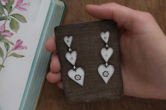 Romantic silver heart earrings with whimsical designs, connected by graceful jump rings for a charming Valentine’s Day accessory.