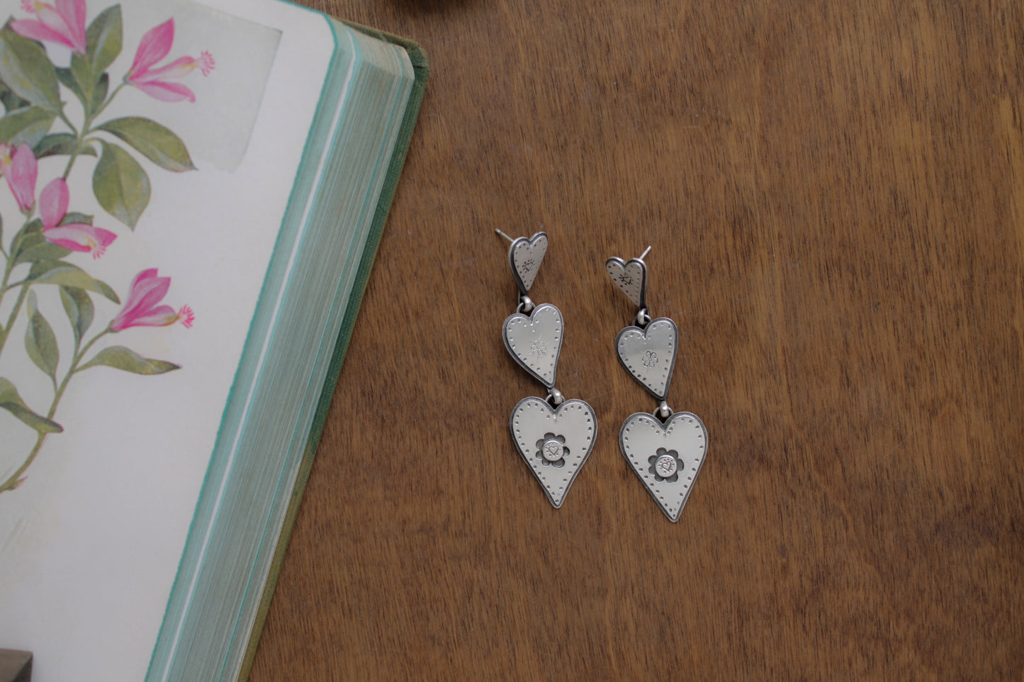 Whimsical sterling silver earrings with three connected hearts, evoking the sweet nostalgia of daydreaming about first love.