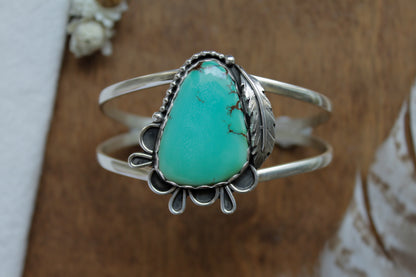 Handmade Turquoise Feather Statement Cuff with Iron Maiden Turquoise gemstone and scalloped sterling silver bezel. Features intricate lace-inspired silverwork, a delicate feather detail, and split shank design. Sustainable artisan jewelry crafted from recycled sterling silver. Perfect for eco-conscious individuals who love unique, vintage-inspired statement pieces