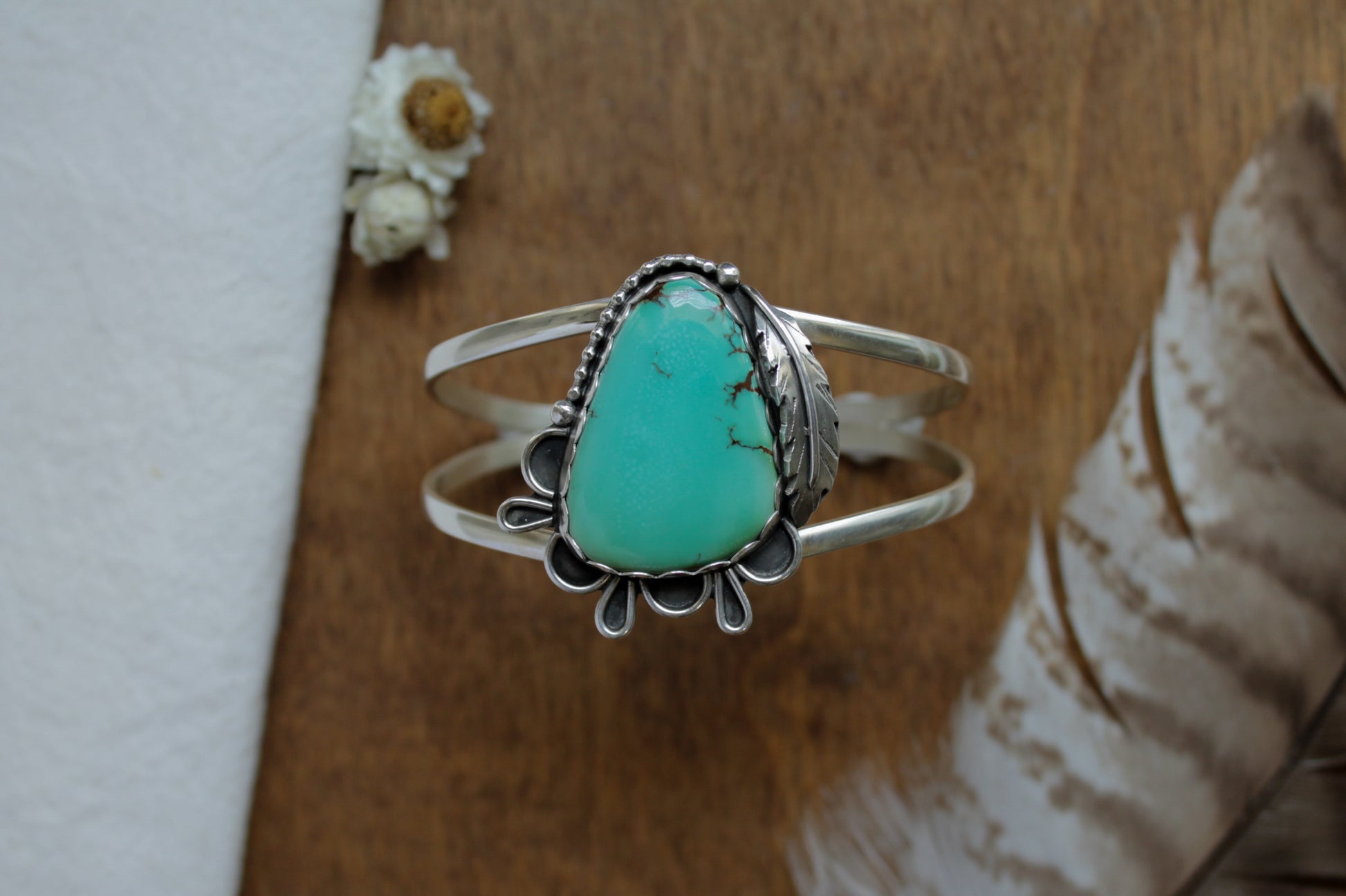 Turquoise Feather Statement Cuff featuring a bold Iron Maiden Turquoise gemstone framed by vintage silver lacework. Includes handmade feather embellishment and hammered adjustable cuff. Crafted from responsibly sourced sterling silver with a sustainable and artistic approach to jewelry design.