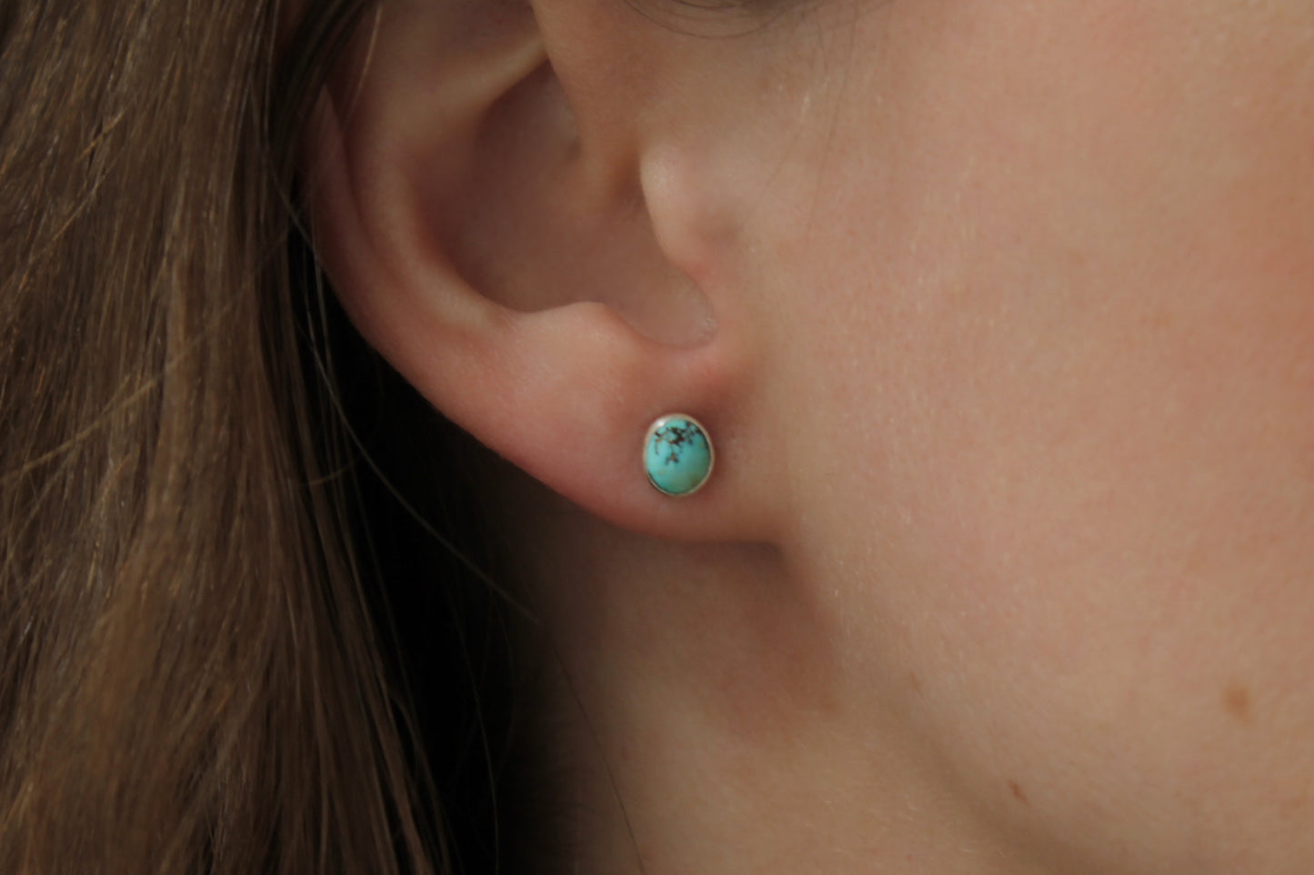 Close-up of an ear wearing a turquoise stud earring.