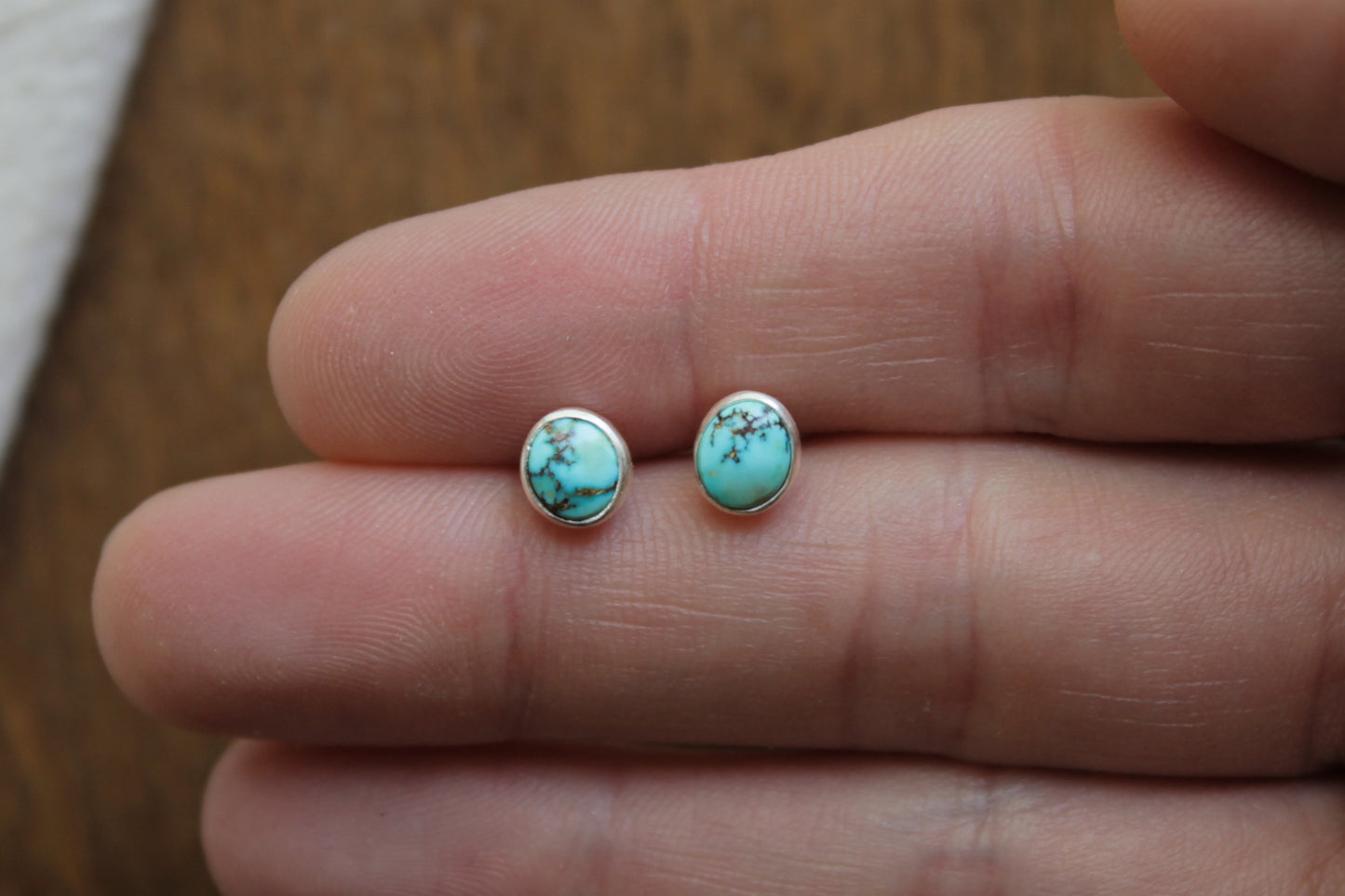 Turquoise stud earrings held between two fingers on a wooden surface