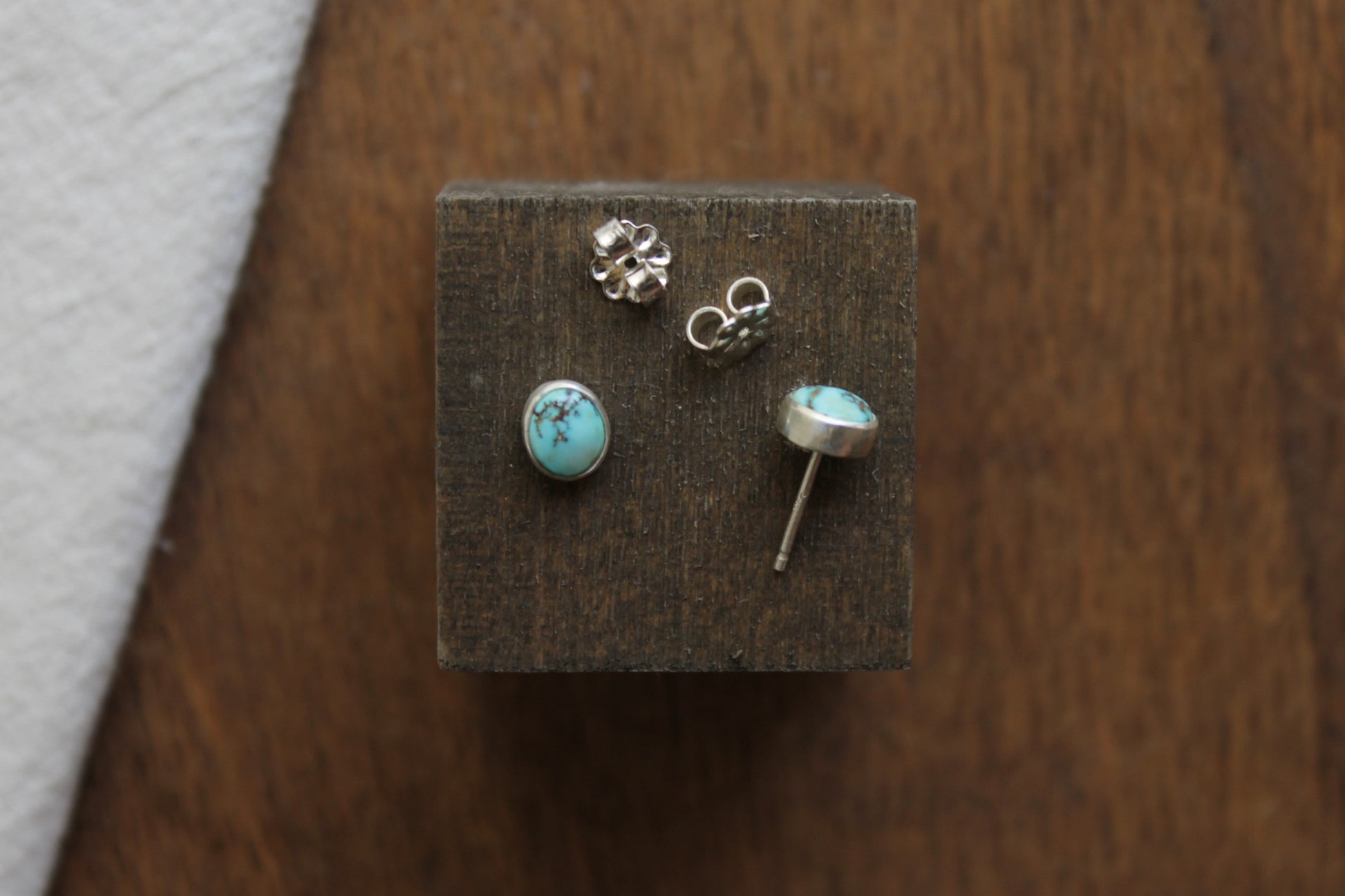Pair of turquoise stone stud earrings on a wooden display block.