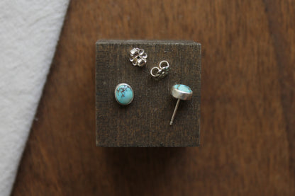 Pair of turquoise stone stud earrings on a wooden display block.