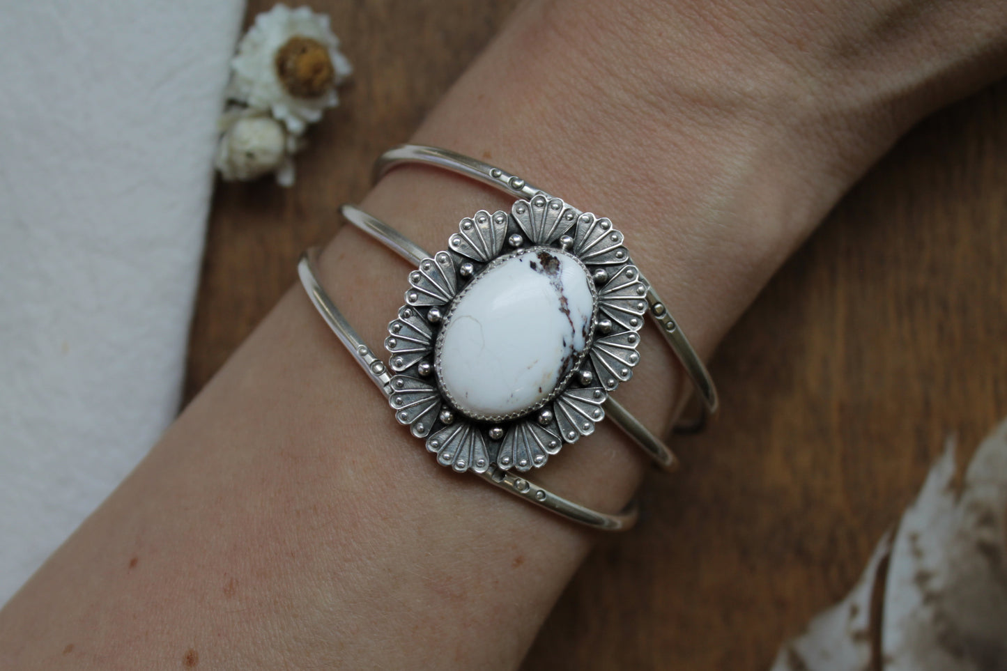 Artisan White Buffalo cuff bracelet in recycled sterling silver with handstamped sunburst design. Boho Western statement jewelry showcasing detailed silverwork, crown-like medallion setting, and adjustable band. Unique handmade silver cuff for the conscious collector