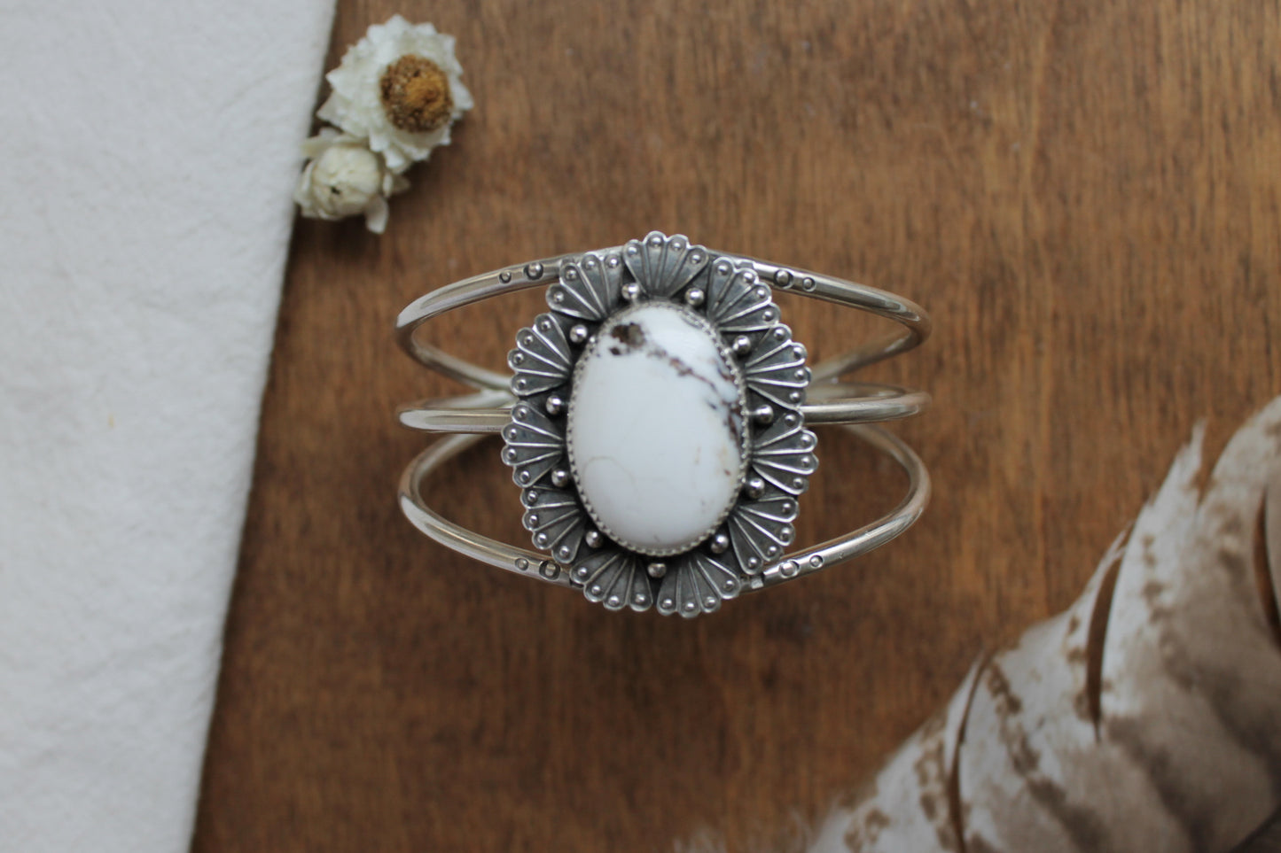 Handmade sterling silver statement cuff bracelet featuring genuine White Buffalo gemstone surrounded by intricate Art Deco fan stampwork. Western bohemian jewelry design with detailed silversmith work including serrated bezel setting, beaded accents, and satin finish. Sustainable artisan jewelry perfect for modern bohemian style.