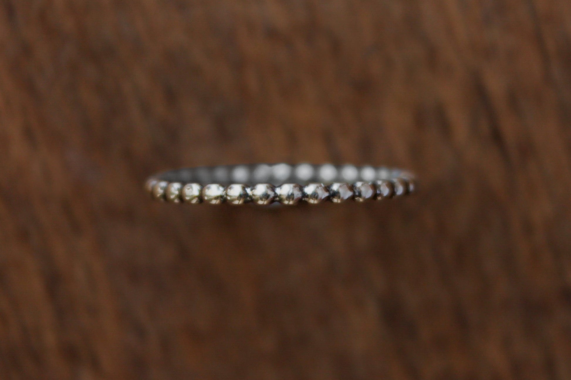 Handmade sterling silver stacker ring with a beaded pattern on a wooden surface