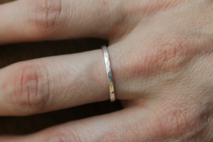 Close-up of a hand wearing a hammered sterling silver ring on a plain background