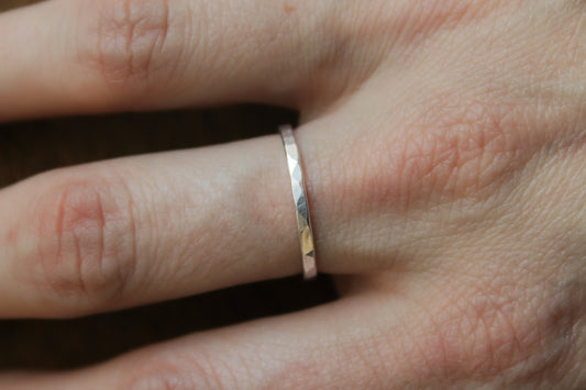 Close-up of a hand wearing a hammered sterling silver ring on a plain background