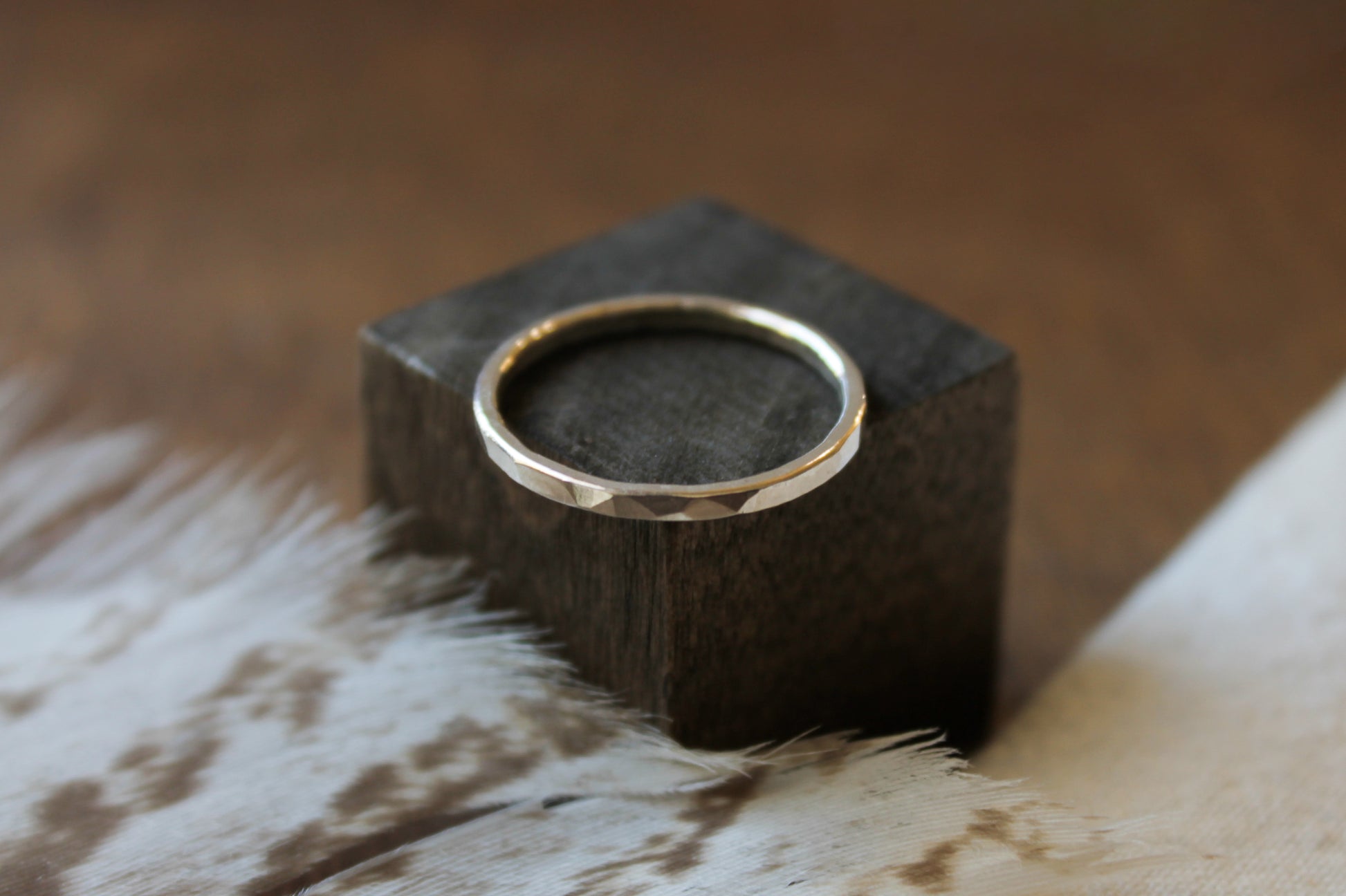 Sterling silver hammered ring on a dark wooden block with a blurred background