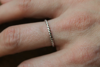 Close-up of a hand wearing a delicate twisted rope sterling silver ring on a blurred background