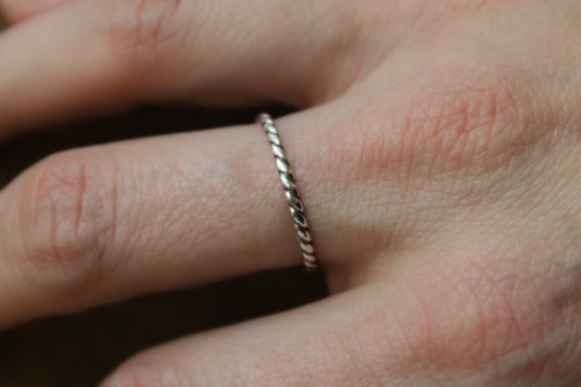 Close-up of a hand wearing a delicate twisted rope sterling silver ring on a blurred background