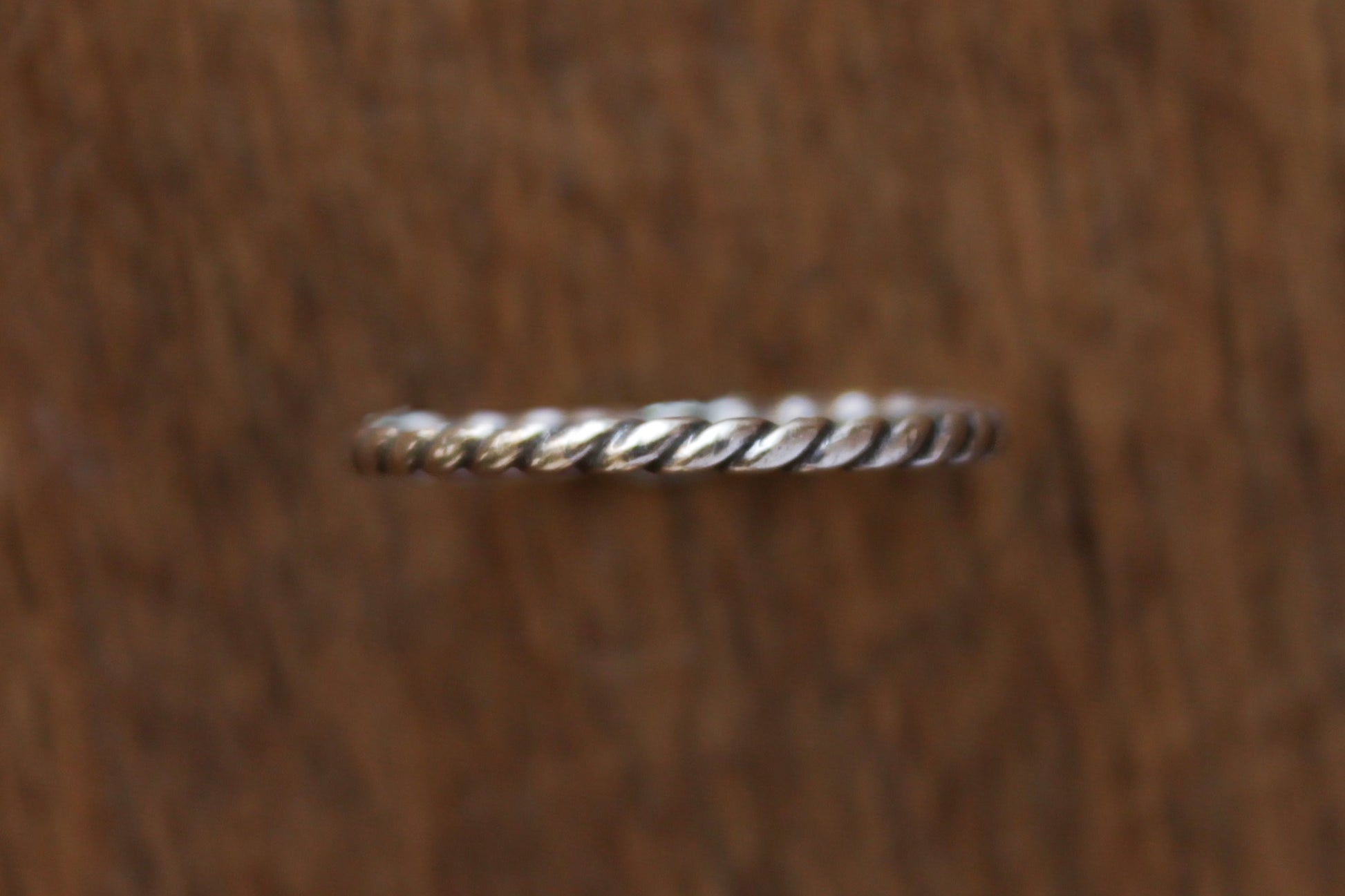 Handmade sterling silver ring with twisted rope design on a wooden surface