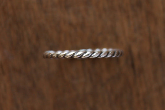 Handmade sterling silver ring with twisted rope design on a wooden surface