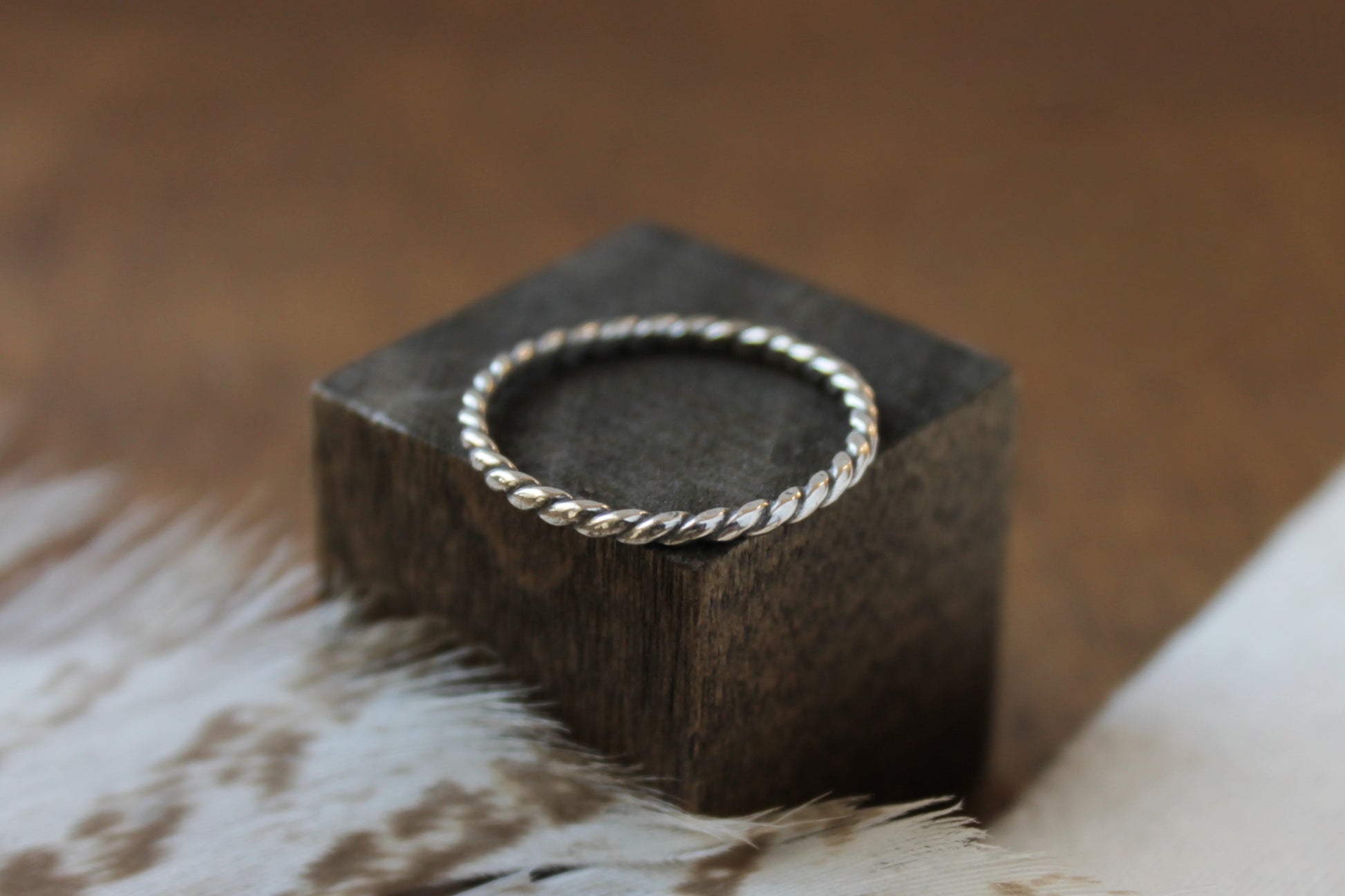 Handmade sterling silver stacker ring on a dark wooden block with a blurred background